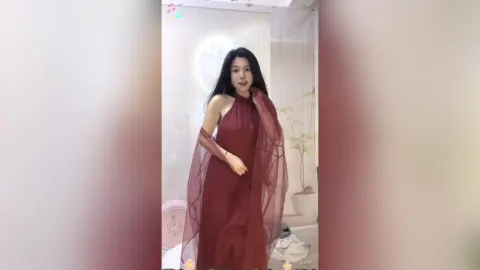 KireliaYan — KireliaYan stands in a room wearing a long, flowing burgundy halter dress.