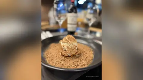 Gourmet dessert topped with light cream and brown powder served in a dark bowl at a fine dining restaurant.