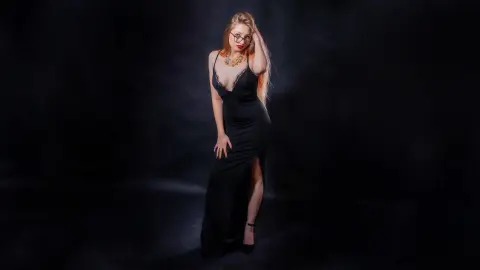 Elegant woman in a black evening gown posing against a dark studio background for a moody portrait.