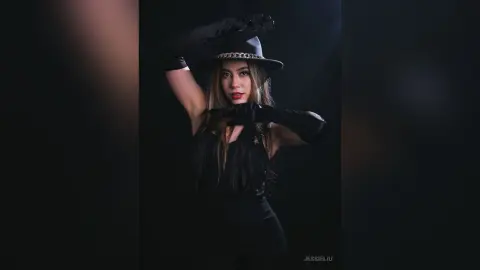 JessieLiu poses in black gloves and a black outfit against a dark background, resting her hand near her face.
