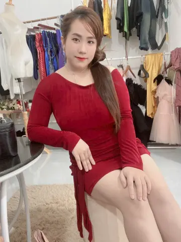 Young woman in a red long-sleeved dress sitting in a clothing boutique with racks of fashion apparel.