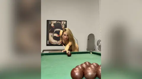 Blonde woman in a black tank top playing billiards in a modern room with a moody atmosphere.