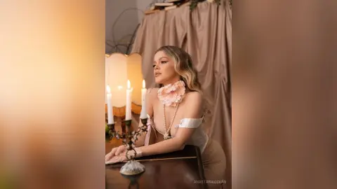 Elegant woman in a white floral couture dress posing by candlelight in a dreamy, romantic indoor setting.