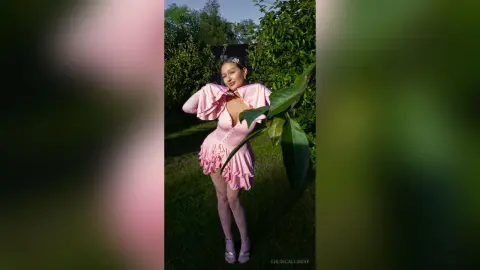 Smiling woman in a pink ruffled mini dress posing in a lush green garden during golden hour.