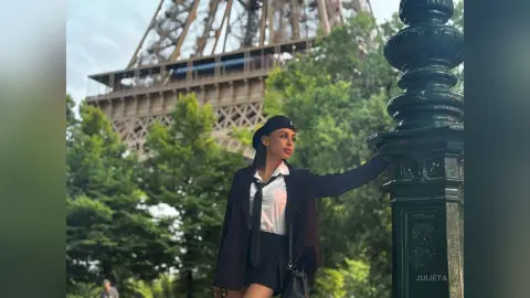 Stylish woman in a black blazer and white shirt posing near the Eiffel Tower in Paris on a sunny day.