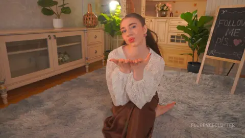 Cheerful young woman in a white lace blouse sitting on a shag rug in a cozy, sunlit living room.