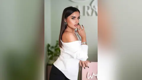Elegant woman in a white off-the-shoulder blouse and silver jewelry posing in a bright, modern studio.
