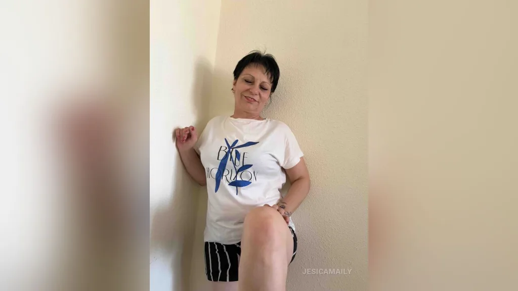 JesicaMaily — JesicaMaily leans against a white wall wearing a white graphic t-shirt and black striped shorts.