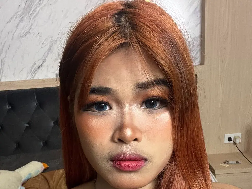 Close-up portrait of a woman with red hair and glowing makeup looking thoughtfully at the camera indoors.