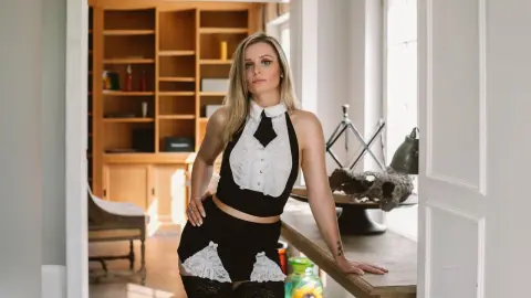 Gia stands in a bright room wearing a black and white lace halter top and matching black lace shorts.