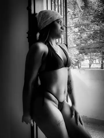 Charlotte_fuentes wearing a bikini and bandana, posing by a window in a black and white photo.