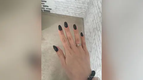 Close-up of a hand with elegant black manicure and silver ring against a white brick wall background.