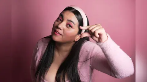 Smiling woman in a pink fuzzy sweater and headband posing against a soft pink background with a dreamy mood.