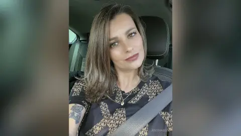 Smiling woman in a patterned black t-shirt sitting in a car interior with a relaxed mood.