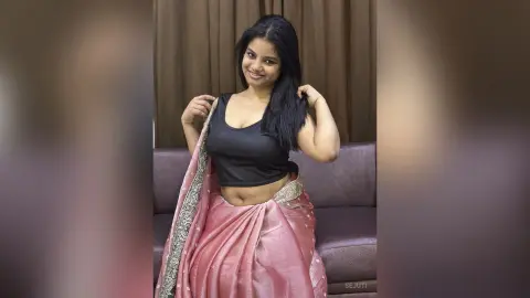 Smiling woman in a pink silk lehenga and black crop top posing indoors with a joyful mood.