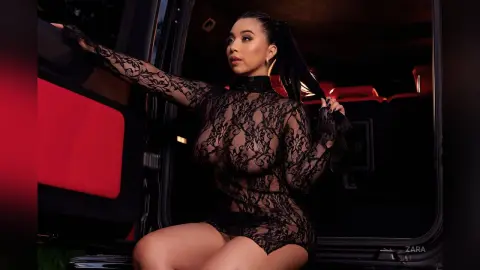 Glamorous woman in a black lace sheer dress posing inside a luxury vehicle at night.