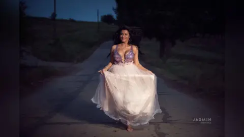 MissyJolie smiles while wearing a light pink lace bustier and a flowing tulle skirt on a dark road.