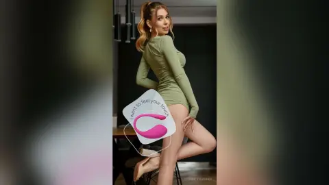 Smiling blonde woman in a tight sage green long-sleeve dress posing in a modern minimalist room.