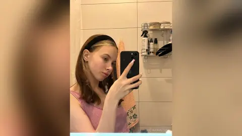 Young woman in a pink tank top taking a casual mirror selfie in a bright bathroom.