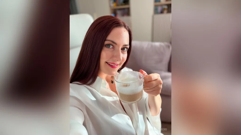 VarvaraMori — VarvaraMori smiles while holding a glass mug of coffee in a white shirt.
