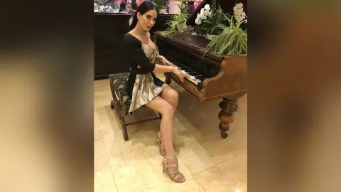 Elegant woman in a gold sequin dress playing a grand piano in a luxurious indoor setting.