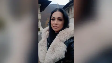Elegant woman in a cozy white faux fur coat posing outdoors near classical architecture.