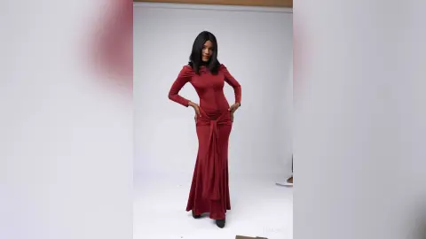 Elegant woman in a long-sleeved burgundy maxi dress posing in a bright white studio setting.