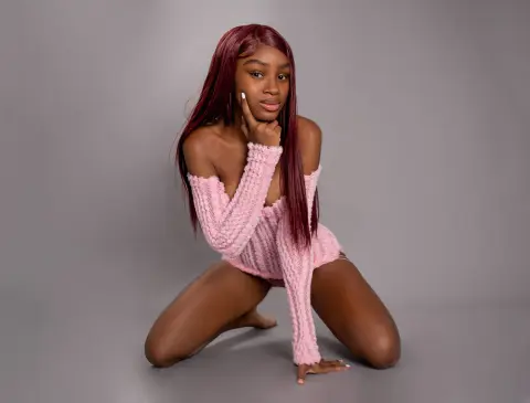 Young woman with long red hair wearing a cozy pink knit sweater posing against a gray studio background.