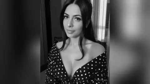 Elegant woman in a polka dot off-the-shoulder dress posing for a moody black and white portrait.