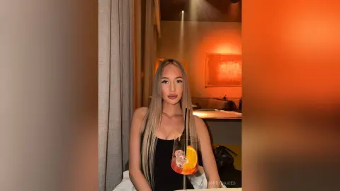 MarryDavies poses in a black tank top while holding a cocktail glass with an orange slice.