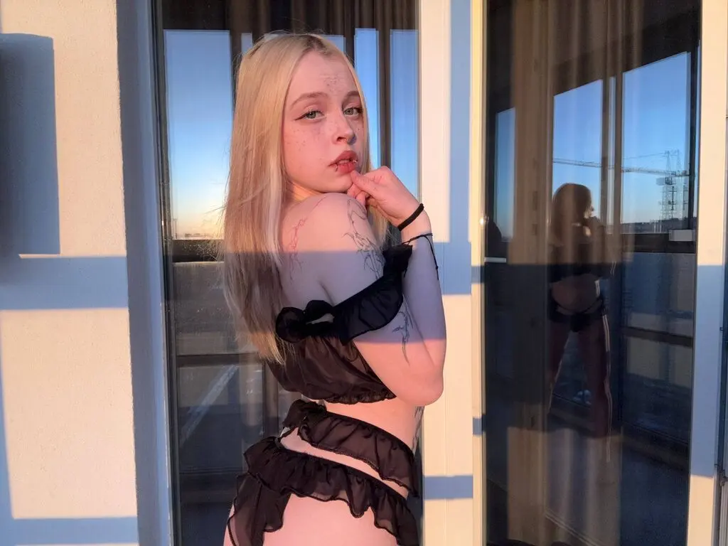 Blonde woman in black ruffled lingerie posing by a window during a warm golden hour sunset.