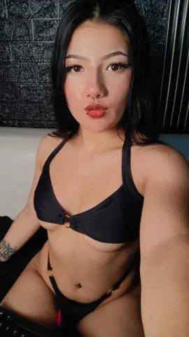 Young woman with long dark hair wearing a black bikini in a modern indoor setting.