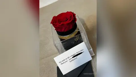 A single red rose in a clear box with a handwritten note from KimRoberth that says, 'You make my life a happier, better place. Thank you!'