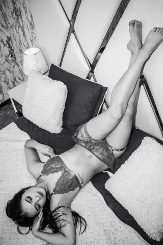 Young woman in lace lingerie relaxing on a bed in a cozy, moody bedroom setting.