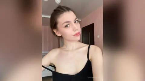 Young woman in a black camisole tank top posing with a soft, natural look in a bright indoor setting.