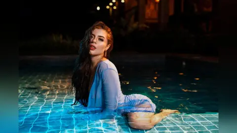 Beautiful woman in a light blue swimsuit relaxing in a glowing swimming pool at night.