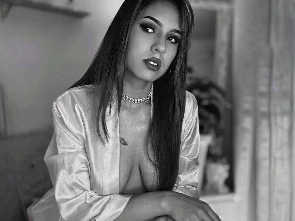 IrinaVal — IrinaVal wears a white satin robe that hangs open to reveal her cleavage and chest, looking directly at the camera with long straight hair.