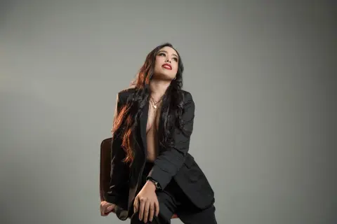 Confident woman in a black blazer sitting against a grey studio background with a sophisticated mood.