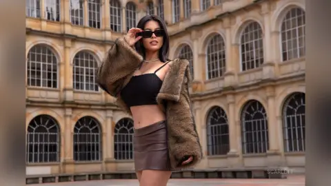 Stylish woman in a brown faux fur coat and black crop top posing in a classic European courtyard.