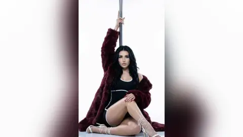 Elegant woman in a black bodysuit and burgundy faux fur coat posing against a white studio background.