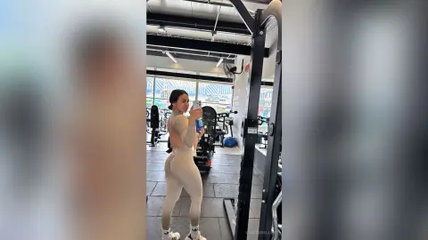 Athletic woman in beige yoga set taking a mirror selfie in a modern bright gym setting.