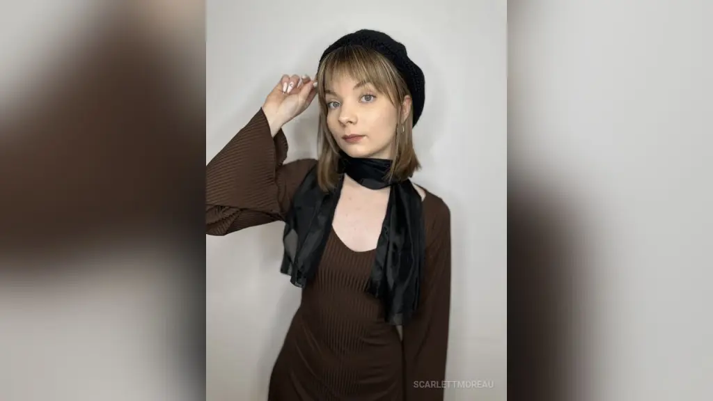 Young woman with blonde bangs wearing a black beanie and brown ribbed sweater in a minimalist studio setting.