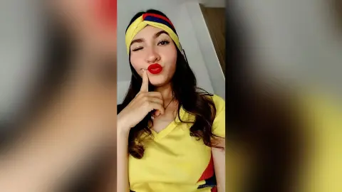 Smiling young woman in a yellow t-shirt and colorful headband winking in a bright indoor setting.