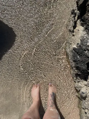 Bare feet resting in clear shallow ocean water on a sunny rocky beach.