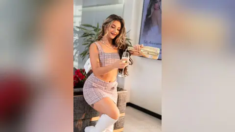 Cheerful woman in a pink plaid two-piece outfit pouring champagne at an upscale indoor celebration.