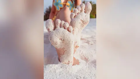 Elie's sandy feet held up against a white sand beach background.