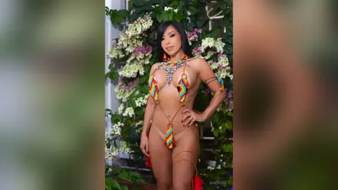 Beautiful woman in colorful tribal beaded bikini posing against a lush floral garden background.