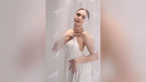 Elegant woman in a white lace slip dress posing gracefully against soft white sheer curtains in a dreamy setting.