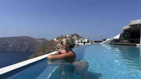 Blonde woman in a swimsuit relaxing in an infinity pool overlooking the ocean in Santorini, Greece.