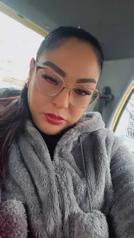 Woman with glasses and makeup wearing a cozy grey fuzzy fleece jacket inside a car.